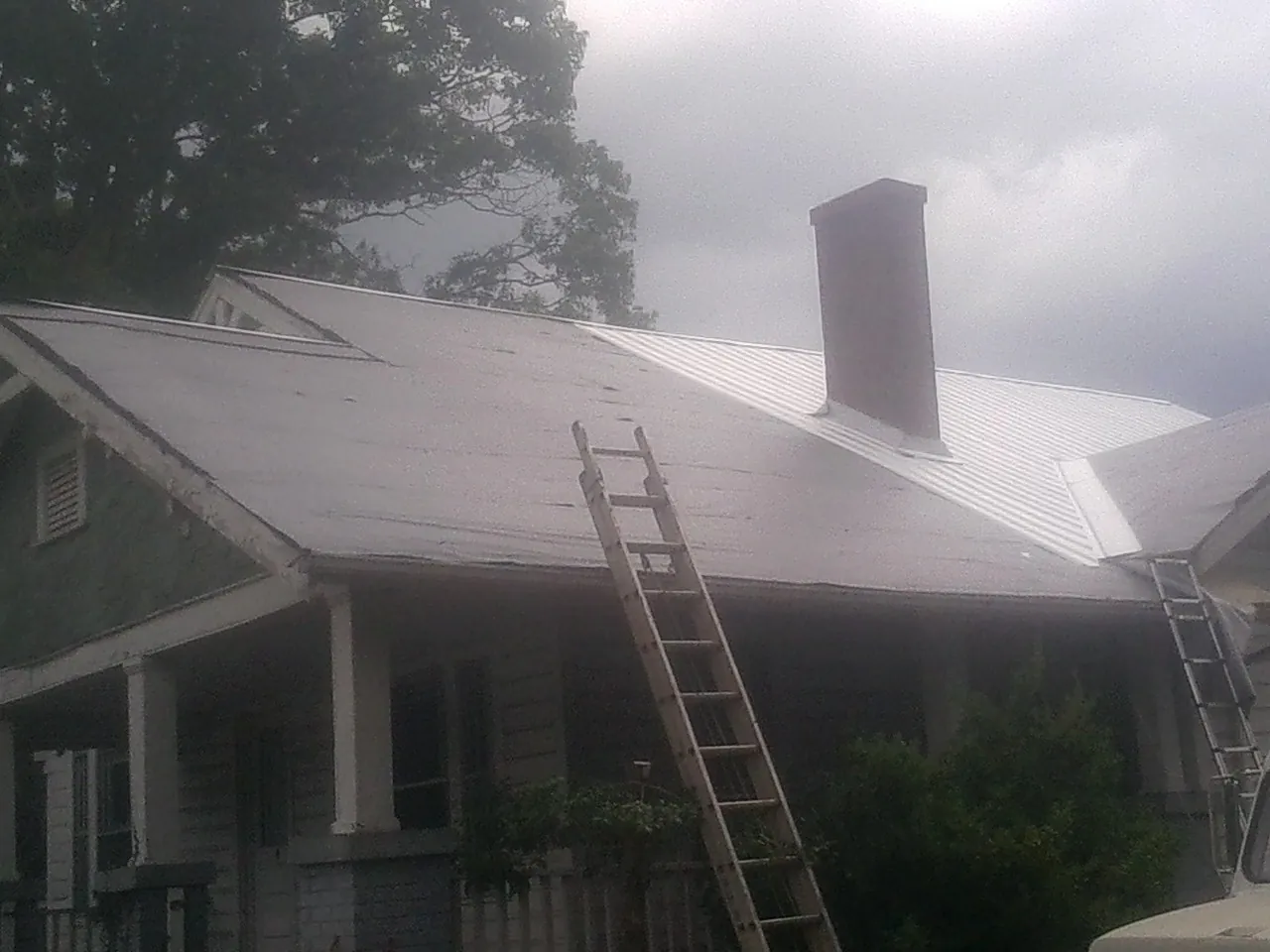 Ladders against a metal roof on an older home with a brick chimney in Dayton